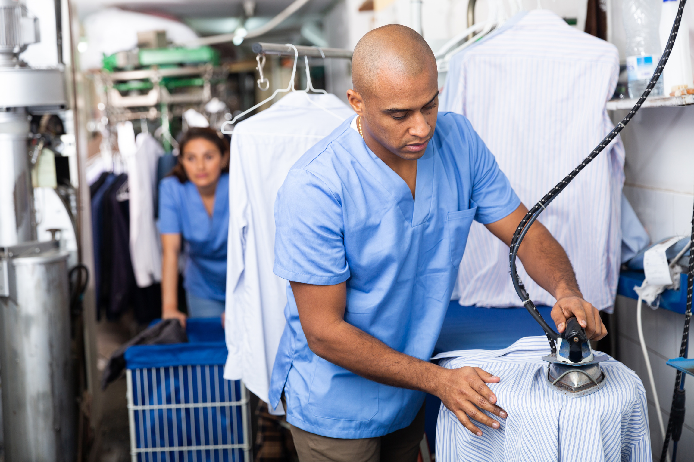 Man laundry worker ironing shirt at dry-cleaning